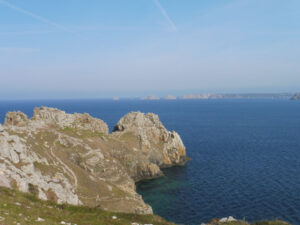 Vue depuis le GR34 sur les falaises déchiquetées de la pointe de Dinan, avec un sentier serpentant entre les rochers de quartzite et en arrière-plan les Tas de Pois dans la brume, presqu'île de Crozon