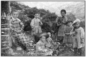 Photographie ancienne en noir et blanc : sept enfants en habits traditionnels posent en plein air dans un cadre montagnard, avec un âne visible à l'arrière-plan.