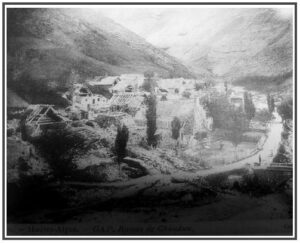 Photographie ancienne en noir et blanc, légendée « Hautes-Alpes — GAP. Ruines de Chaudun » : vue en plongée sur les vestiges du village de Chaudun dans son vallon, charpentes à nu et murs en ruine visibles parmi la végétation, rivière longeant le site.