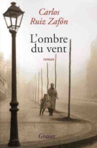 Couverture du roman « L'ombre du vent » de Carlos Ruiz Zafón aux éditions Grasset, avec une photographie sépia d'une rue barcelonaise brumeuse sous un réverbère, où un adulte et un enfant marchent dans le brouillard.