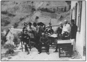Photographie ancienne en noir et blanc : groupe d'une quinzaine de personnes réunies en plein air autour d'une table de travail lors de la signature officielle de la vente du village de Chaudun à l'État, le 24 août 1895.