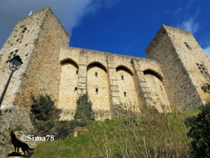 Vue en contre-plongée des remparts et des deux tours carrées du château médiéval de Chevreuse, en pierre calcaire beige, avec trois arcades en plein cintre sur la façade, sous un ciel bleu intense. Photo ©Sima78.