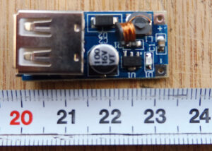 Petit module électronique convertisseur DC-DC boost sur circuit imprimé bleu avec connecteur USB-A femelle, photographié sur une surface en bois avec une règle graduée indiquant une longueur d'environ 4 cm.