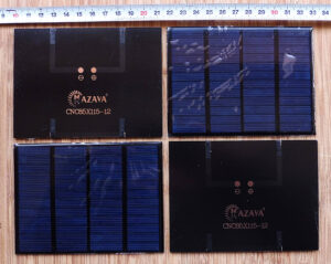 Quatre petits panneaux solaires photovoltaïques Mazava modèle CNC85X115-12 posés sur une surface en bois, présentés recto et verso, avec une règle graduée indiquant environ 85 x 115 mm de dimension.