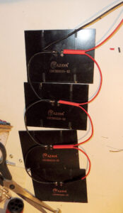 Quatre mini panneaux solaires Mazava CNC85X115-12 face arrière visible, câblés en série avec des fils rouge (positif) et noir (négatif) soudés sur les bornes, posés sur un établi avec des outils électroniques visibles.