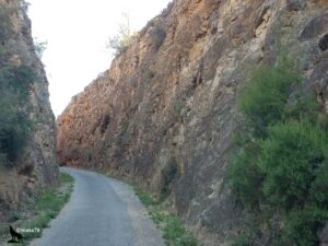 Chemin stabilisé serpentant entre deux hautes parois rocheuses aux teintes ocre et rouille, bordée de végétation arbustive verte, formant un couloir naturel saisissant