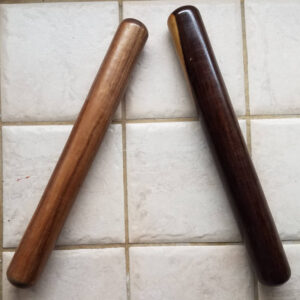 Paire de claves en bois posées en croix sur un carrelage blanc : l'une en bois clair (acajou ou hêtre), l'autre en bois sombre (ébène ou palissandre).