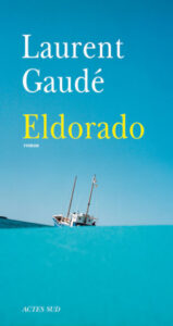 Couverture du livre « Eldorado » de Laurent Gaudé, publié aux éditions Actes Sud. Un voilier blanc est échoué sur une mer turquoise sous un ciel bleu. Le titre est inscrit en jaune, le nom de l'auteur en blanc.