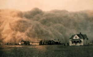 Photographie en sépia d'un gigantesque mur de poussière (black blizzard) s'abattant sur un hameau de maisons blanches en bois dans les Grandes Plaines américaines, vers 1935. Une silhouette humaine se distingue à droite, devant une ferme.