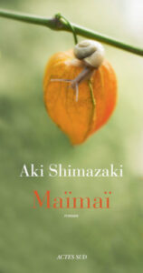 Couverture du roman Maïmaï d'Aki Shimazaki, publié aux éditions Actes Sud, ornée d'une photographie d'un petit escargot perché sur une physalis orange suspendue à sa tige, sur fond vert flou.