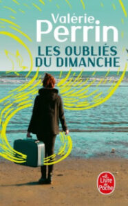 Couverture du roman « Les Oubliés du Dimanche » de Valérie Perrin : une femme de dos, valise à la main, face à une mer agitée sous un ciel nuageux.