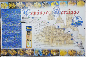 Panneau émaillé du Camino de Santiago installé près de la plage de Puerto de Sagunto, encadré de coquilles Saint-Jacques en céramique jaune et bleue, marquant le km 0 du parcours avec 1 057 km à parcourir jusqu'à Santiago de Compostela, la liste complète des étapes et une illustration de la cathédrale de Compostelle. Mention "Amigos del Camino - Sagunto - Buen Camino".