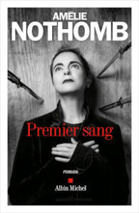 Couverture du roman « Premier sang » d'Amélie Nothomb aux éditions Albin Michel, avec une photographie en noir et blanc de l'auteure entourée de couteaux pointés vers elle, et le titre en rouge.
