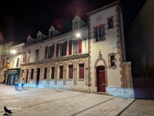 Bâtiment historique en brique et pierre, éclairé la nuit, avec des arcades et des fenêtres à volets rouges, situé Place du Général de Gaulle à Chartres.