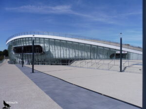 Le Colisée de Chartres, bâtiment moderne en verre et métal de forme ovale, avec des escaliers et une terrasse, sous un ciel bleu dégagé.