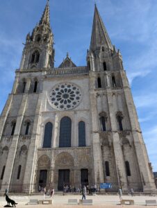 Façade de la Cathédrale Notre-Dame de Chartres, avec ses deux flèches, sa rosace, ses portails sculptés et ses vitraux, sous un ciel bleu avec quelques nuages.