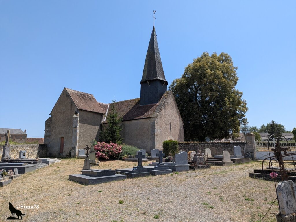 Photographie de l'église Saint-Hilaire de La Motte-Feuilly, édifice en pierre surmonté d'un clocher pointu à ardoises, entourée du cimetière communal, sous un ciel bleu dégagé.