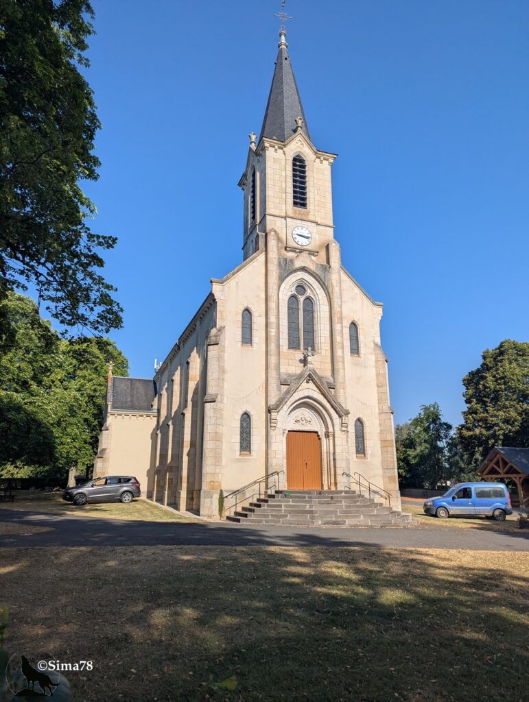 Photographie de l'église Saint-Pierre-et-Saint-Paul de Sidiailles, édifice néogothique en pierre claire avec clocher à flèche élancée surmonté d'une croix et orné d'une horloge, sous un ciel bleu dégagé.