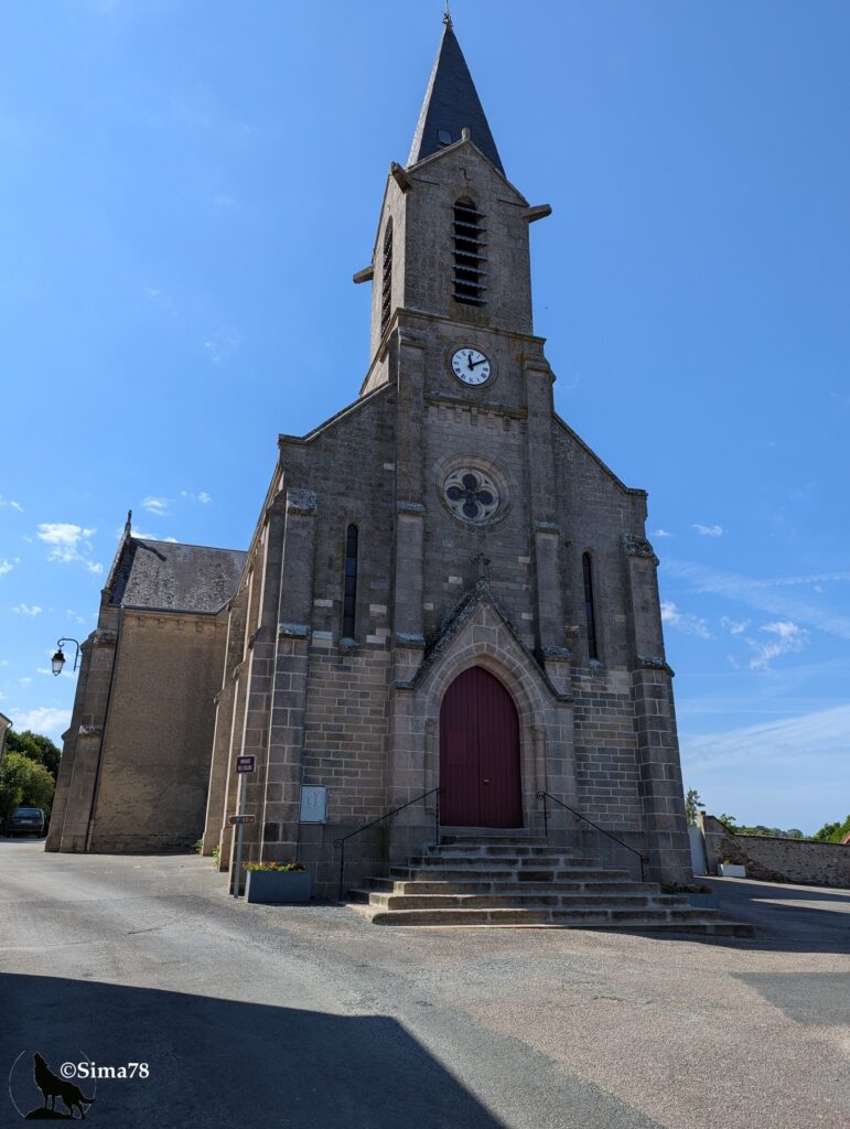 Photographie de l'église Sainte-Désirée de Pérassay, édifice en pierre avec clocher à flèche d'ardoise, horloge et rosace, sous un ciel bleu dégagé.